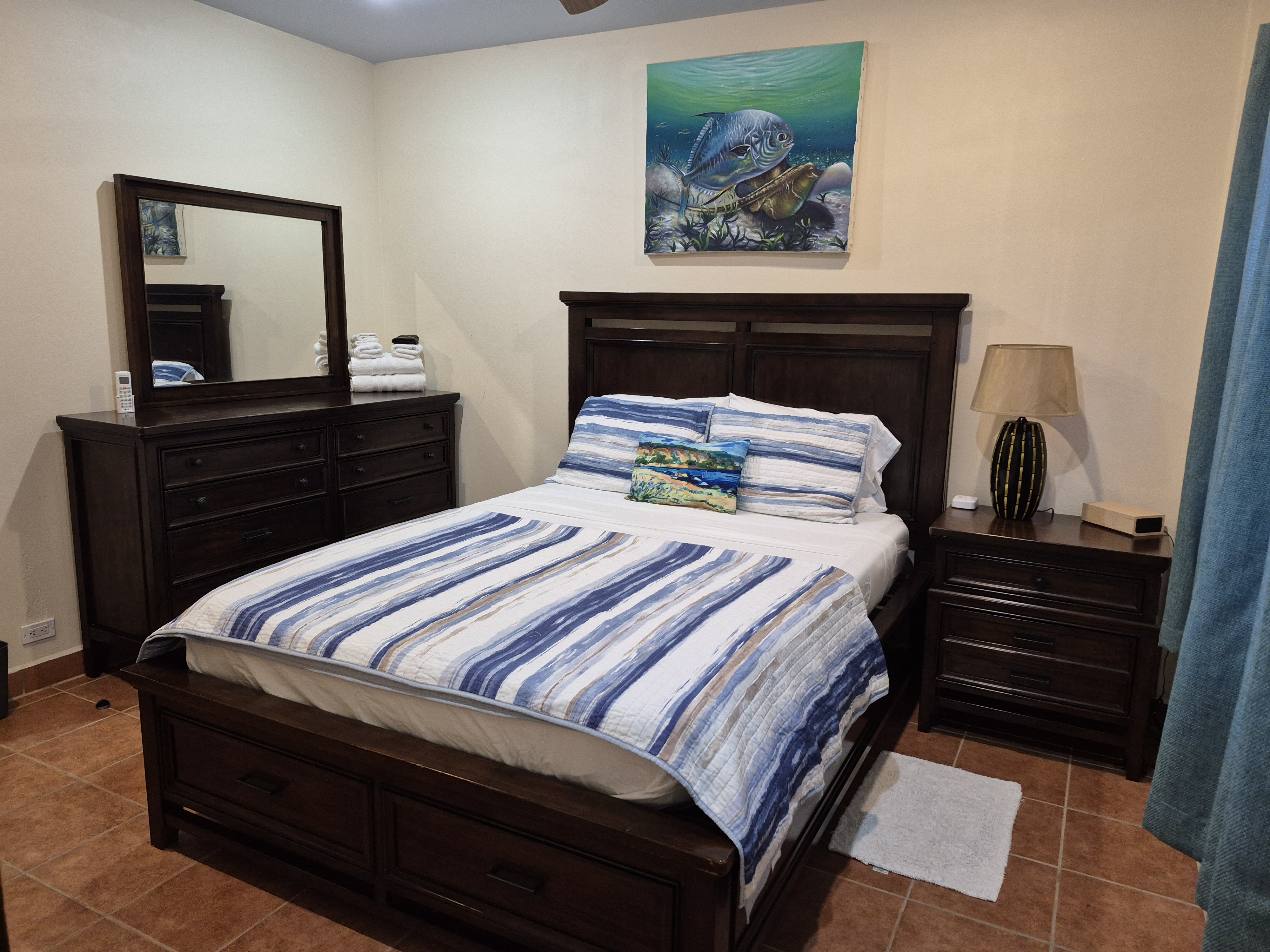 Bedroom with a dark wood queen bed, dresser with mirror, nightstand with lamp, and blue and white striped bedding.