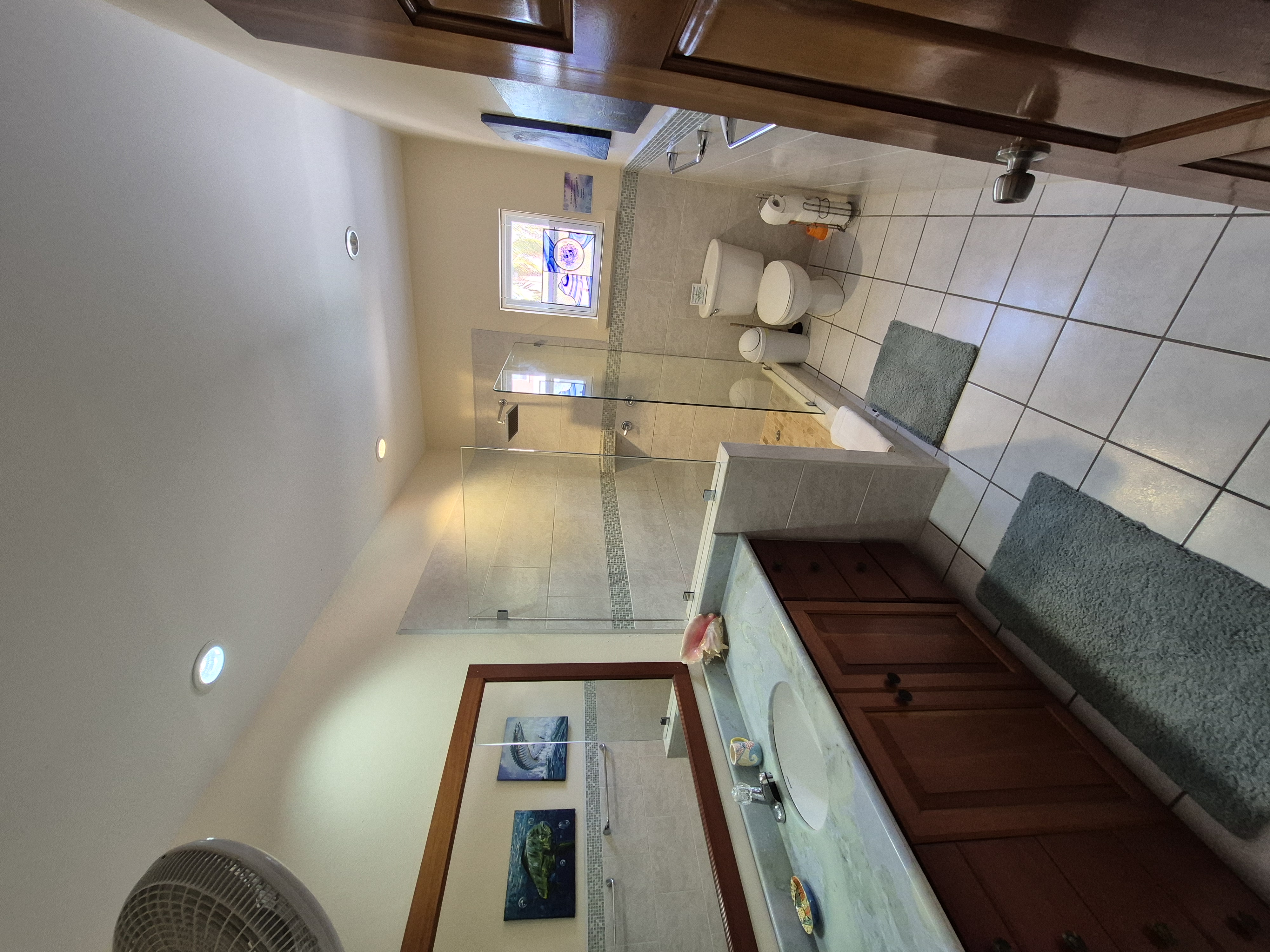 Spacious bathroom with a double sink vanity with wooden cabinets and a light countertop, a large rectangular mirror, a glass-enclosed shower, and a toilet.