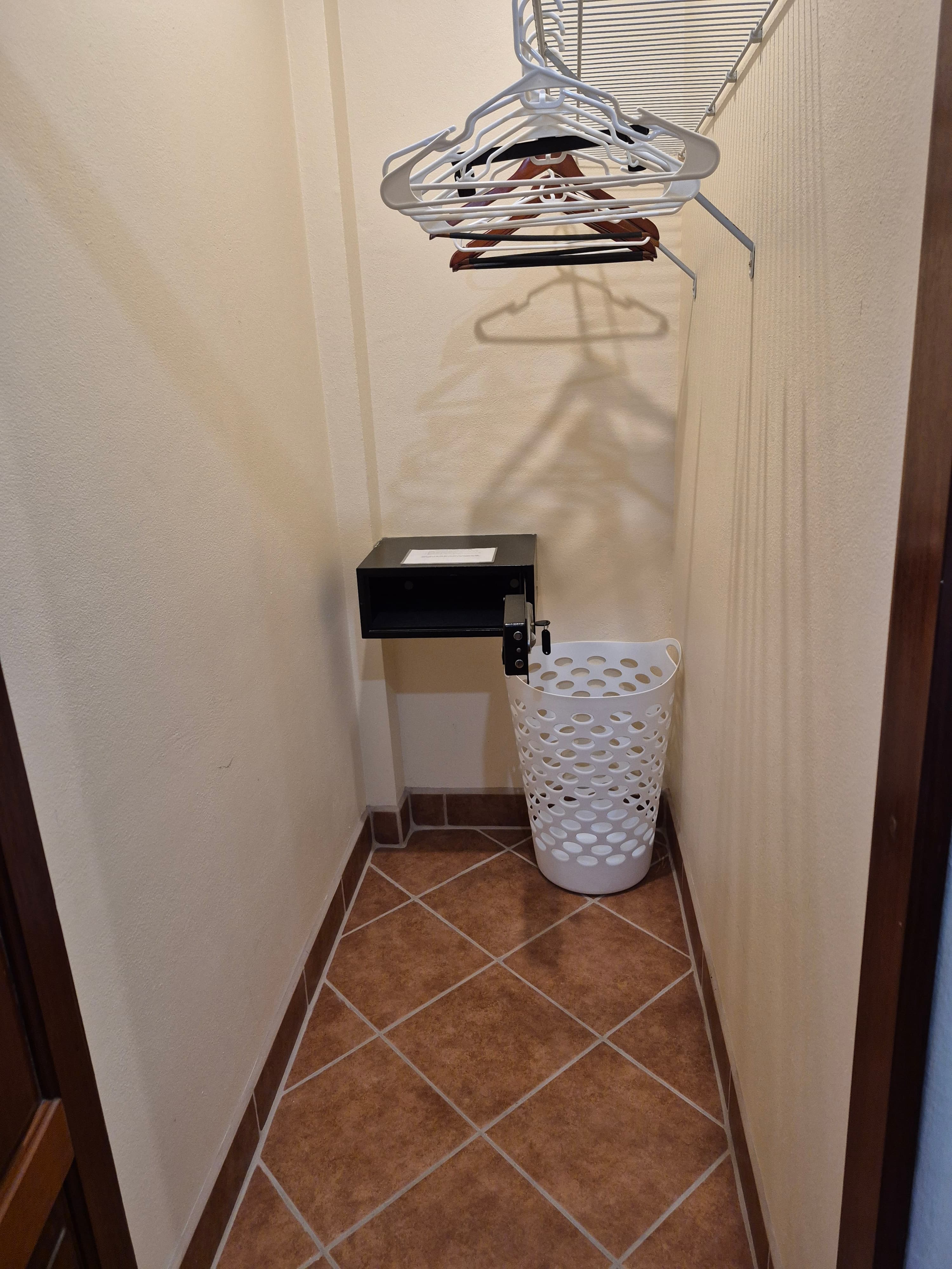 Closet with hanging rack & hangers, laundry hamper, and brown tiled floor.