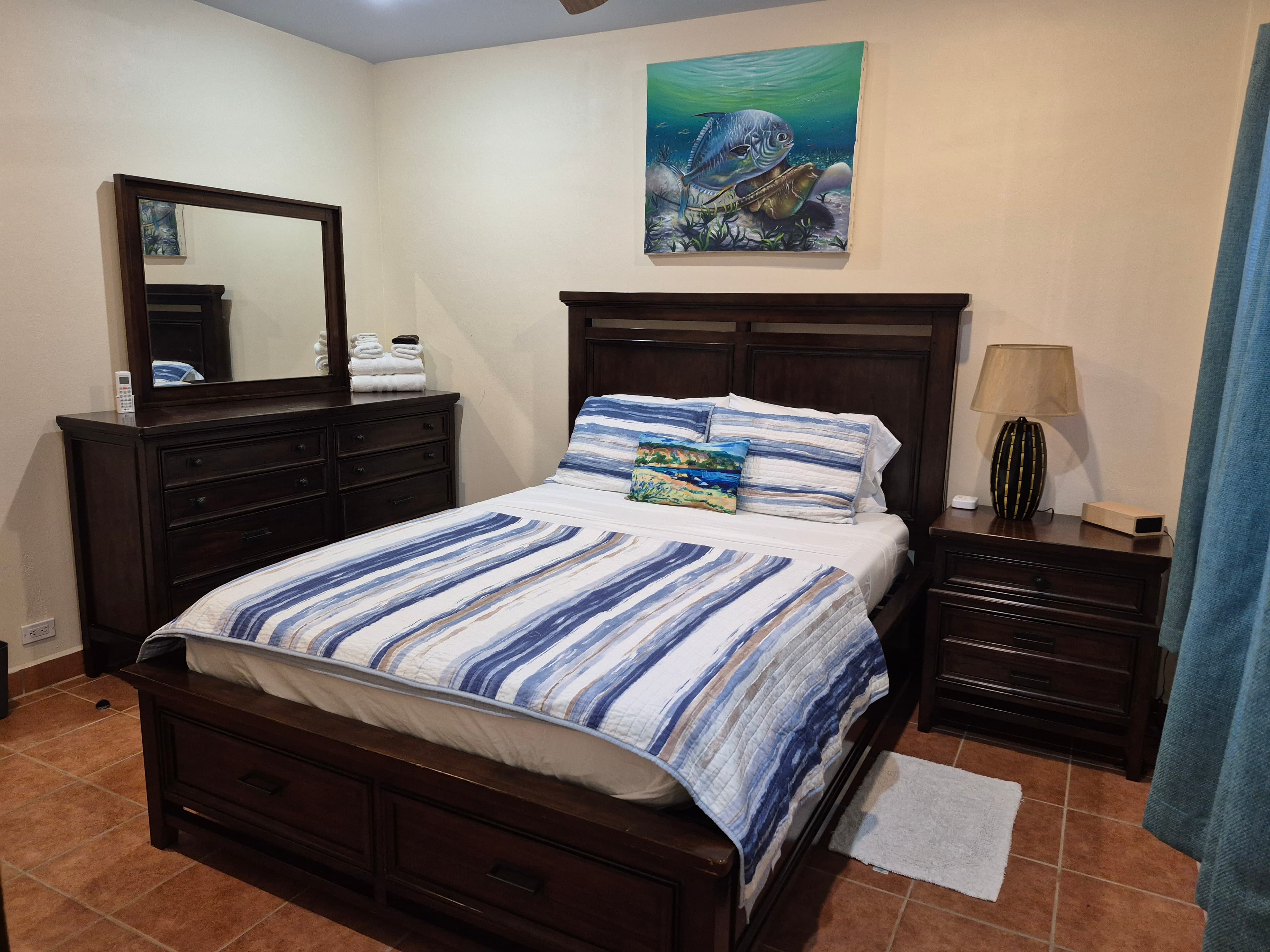 Bedroom with a dark wood queen bed, dresser with mirror, nightstand with lamp, and blue and white striped bedding.