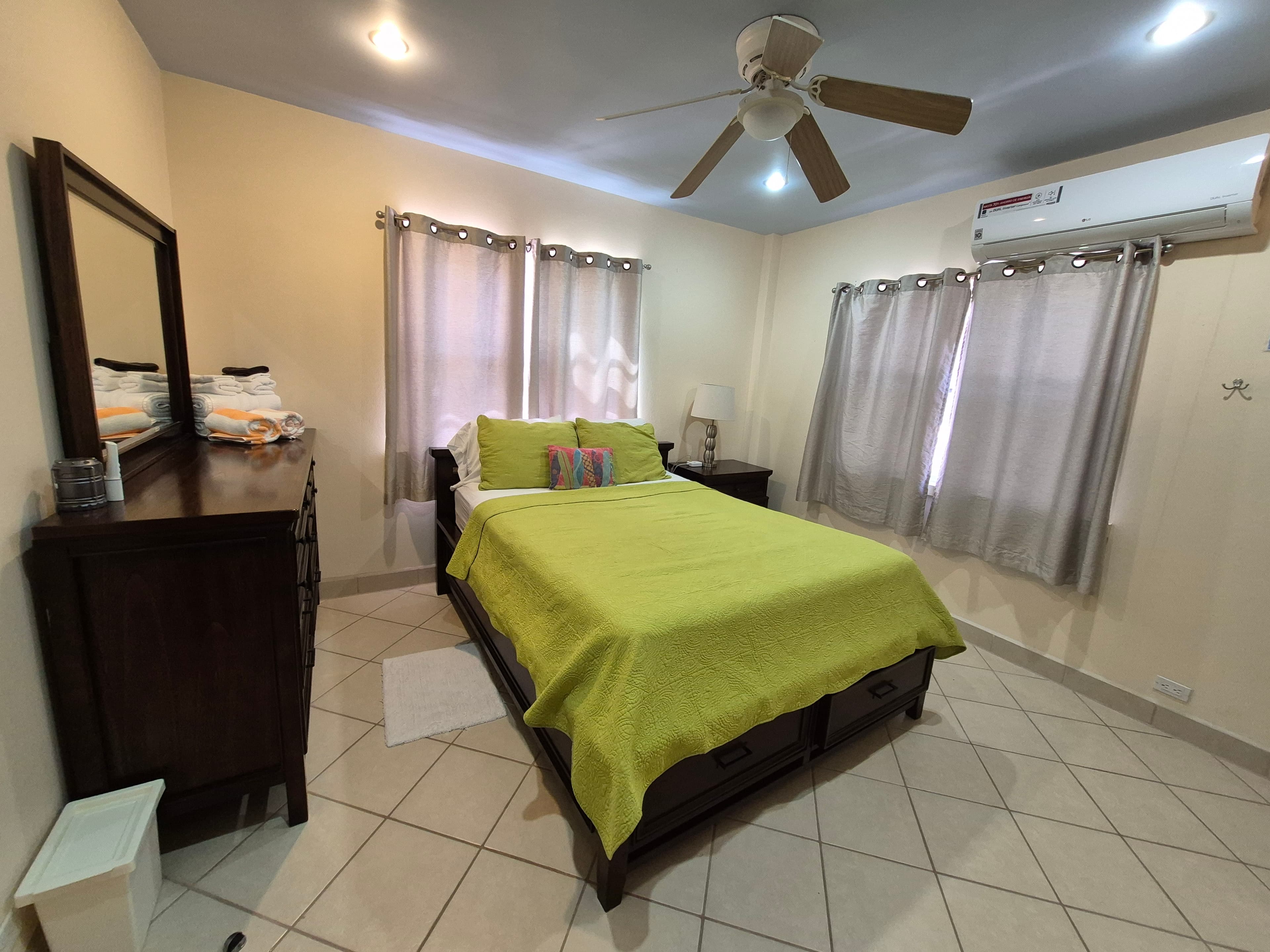 Bedroom with a dark wood queen bed dressed in a lime green blanket and pillows, a dark wood dresser with a mirror, and a dark wood nightstand.