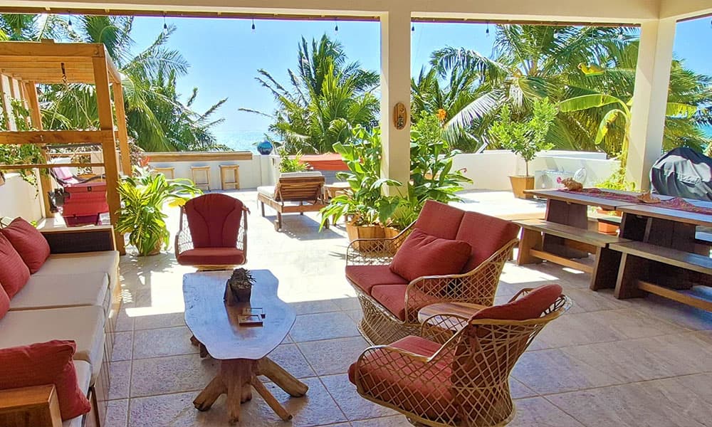 A bright, open patio featuring comfortable seating, lush greenery, and a view of the ocean.