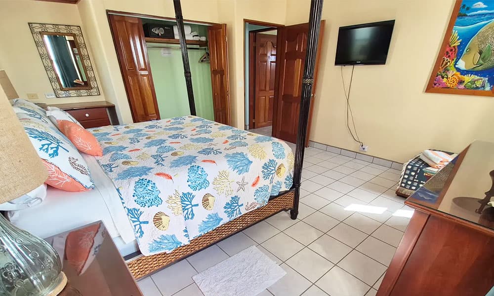 A bright and cozy bedroom featuring a four-poster bed, colorful bedding, and a wall-mounted TV.